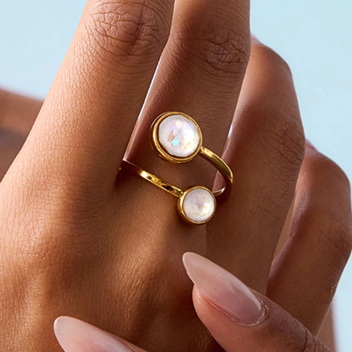 A gold ring with a pearl and a stone worn on the finger