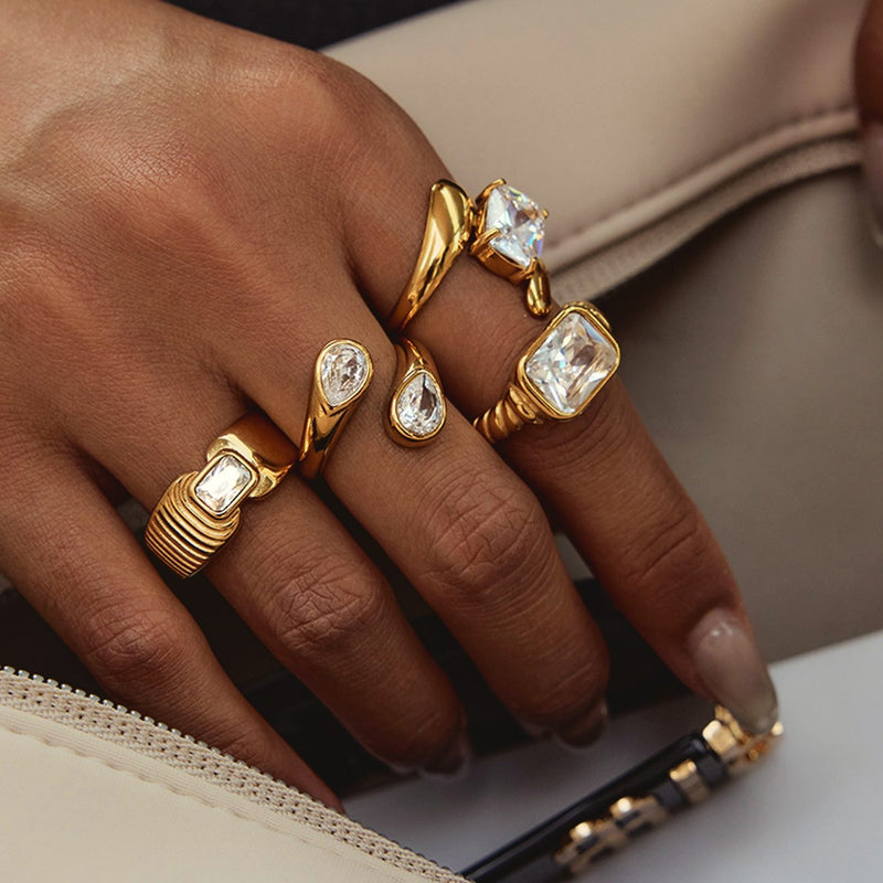 A hand wearing several gold rings with coloured stones